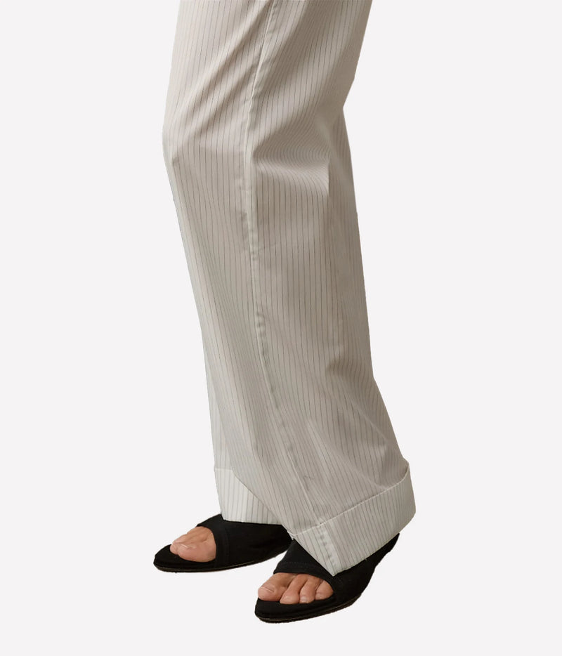 Close-up of a person's lower legs wearing off-white pinstriped trousers and black open-toe slide sandals against a plain light gray background.