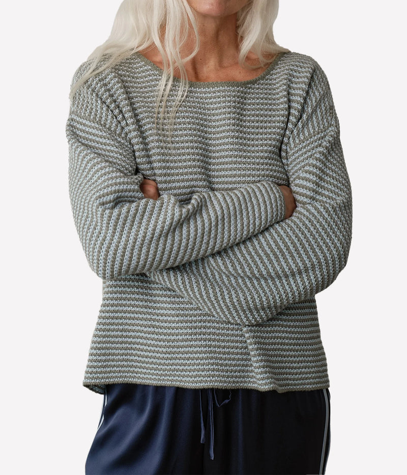 A woman wearing a textured knit sweater with horizontal gray and white stripes, paired with dark navy pants, shown from the neck down against a light gray background.