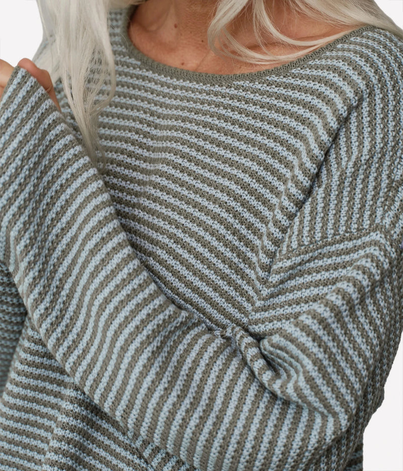 Close-up of a person wearing a knit sweater with narrow horizontal stripes in muted sage green and light gray, with blonde hair visible at the neckline.