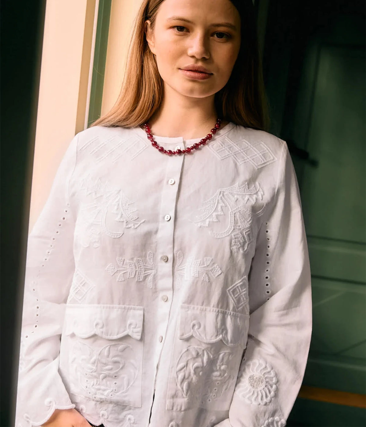 Model wearing the Sissel Edelbo Ester Shirt in Ecru buttoned, with a red beaded necklace, showing the relaxed fit and embroidered cutwork detail