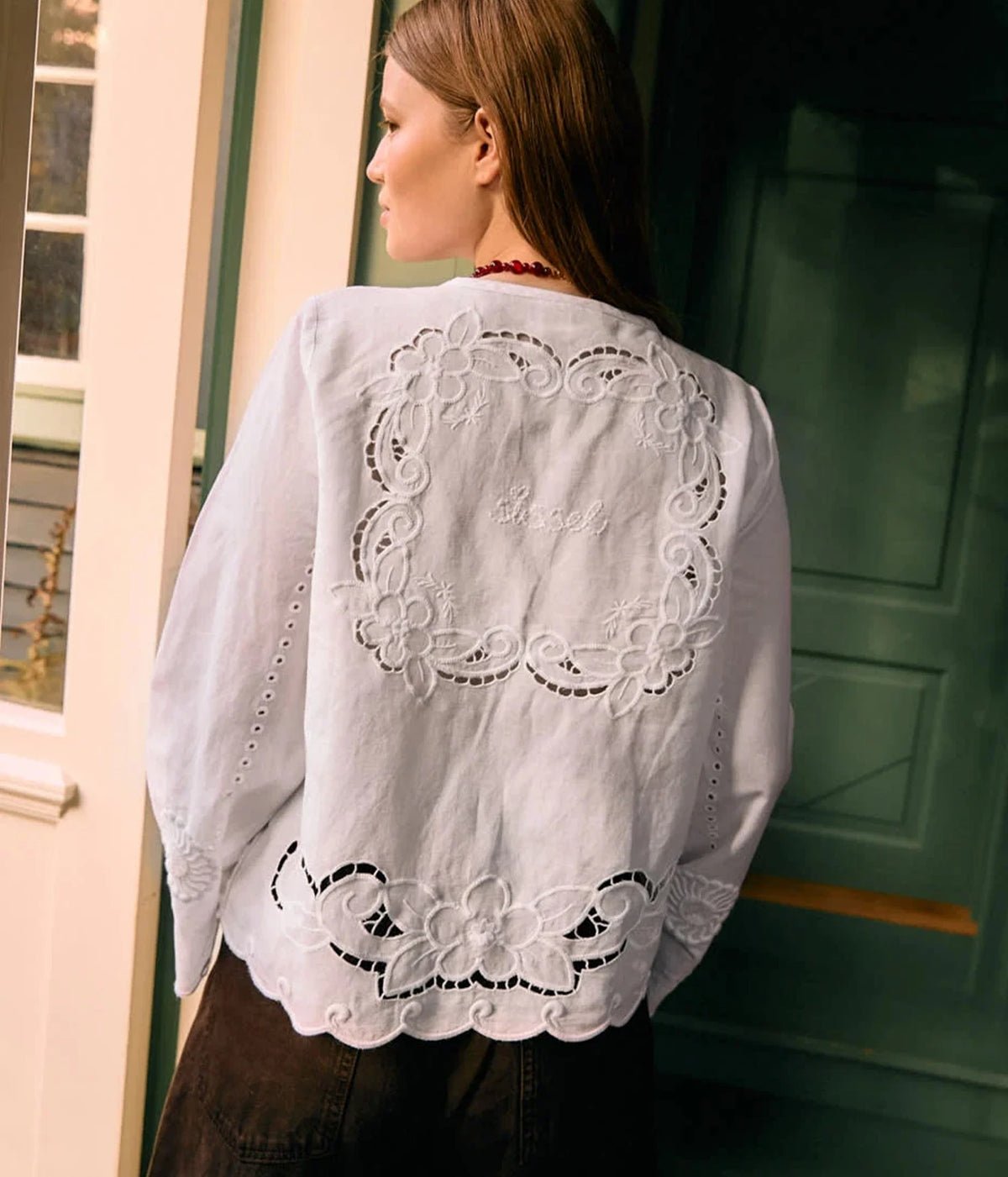 Back view of a model wearing the Sissel Edelbo Ester Shirt in Ecru with a dark skirt, showing the embroidered cutwork motif across the back and the scalloped hem