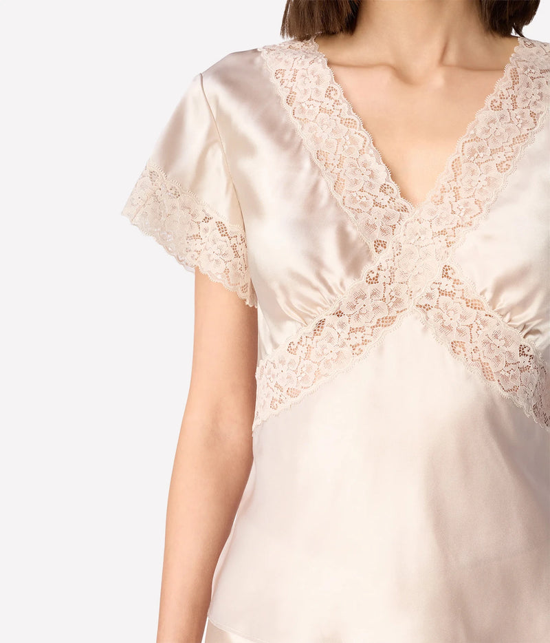 A close-up of a woman wearing a light cream satin top with lace trim along the V-neckline and short sleeves.