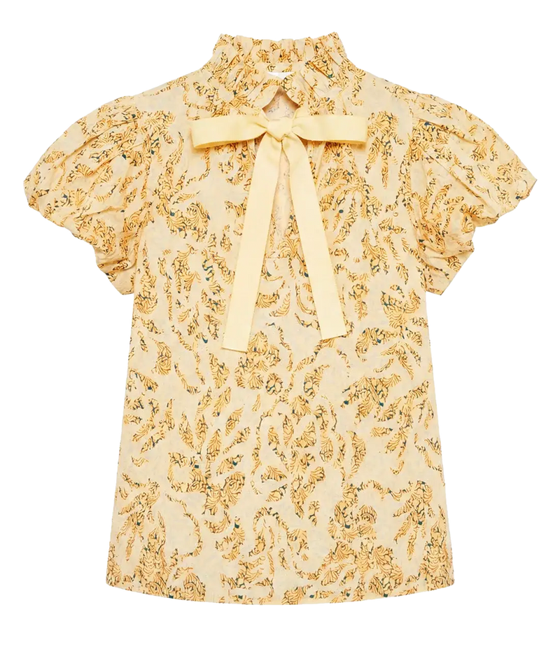 A short-sleeve blouse with a high collar, ruffled sleeves, and a large bow at the neckline, featuring an all-over yellow and green botanical print on a light cream background.