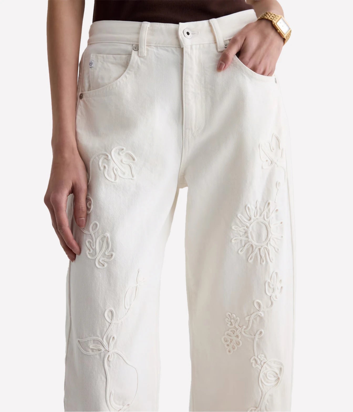 A close-up of a person wearing off-white embroidered jeans with floral cutwork details, shown from the waist down against a plain light background.