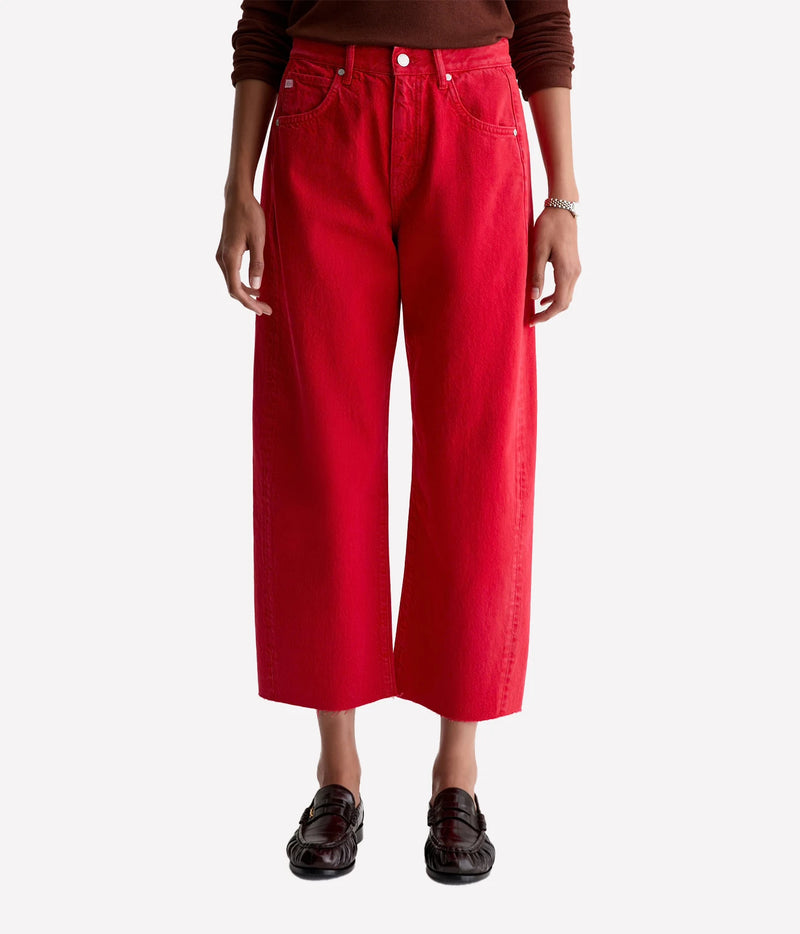 Front view of a model wearing the AG Hattie Crop in Recording Red with a brown knit top tucked in, a silver watch and dark brown leather loafers, showing the barrel leg and cropped length