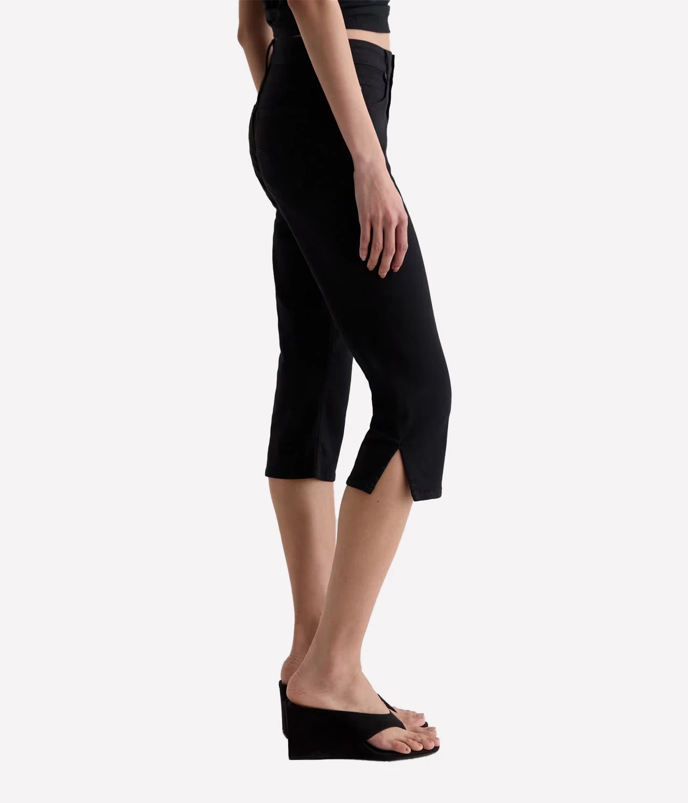 A model shown from the waist down wearing black cropped capri pants with side slits and black wedge slide sandals, set against a plain light gray studio background.