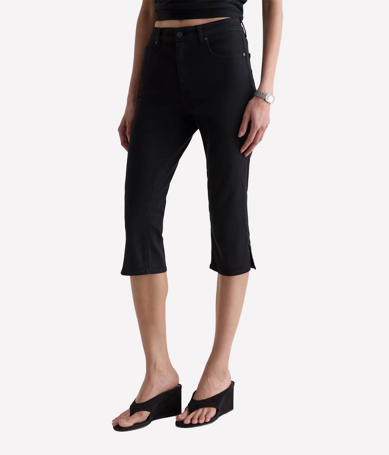 A model wearing black cropped capri jeans with side slits, paired with black wedge sandals and a black top, shown against a light gray studio background.