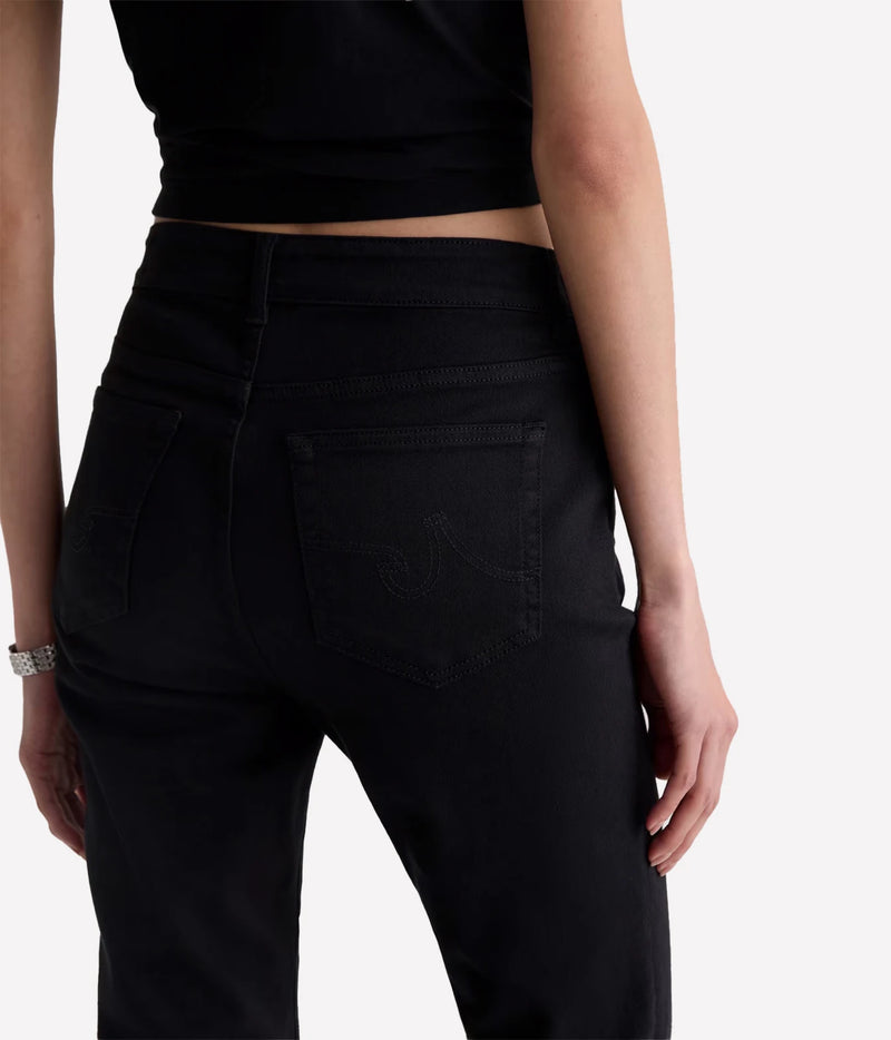 Rear view of a person wearing black high-waisted jeans with a cropped black top, shown against a plain light background.