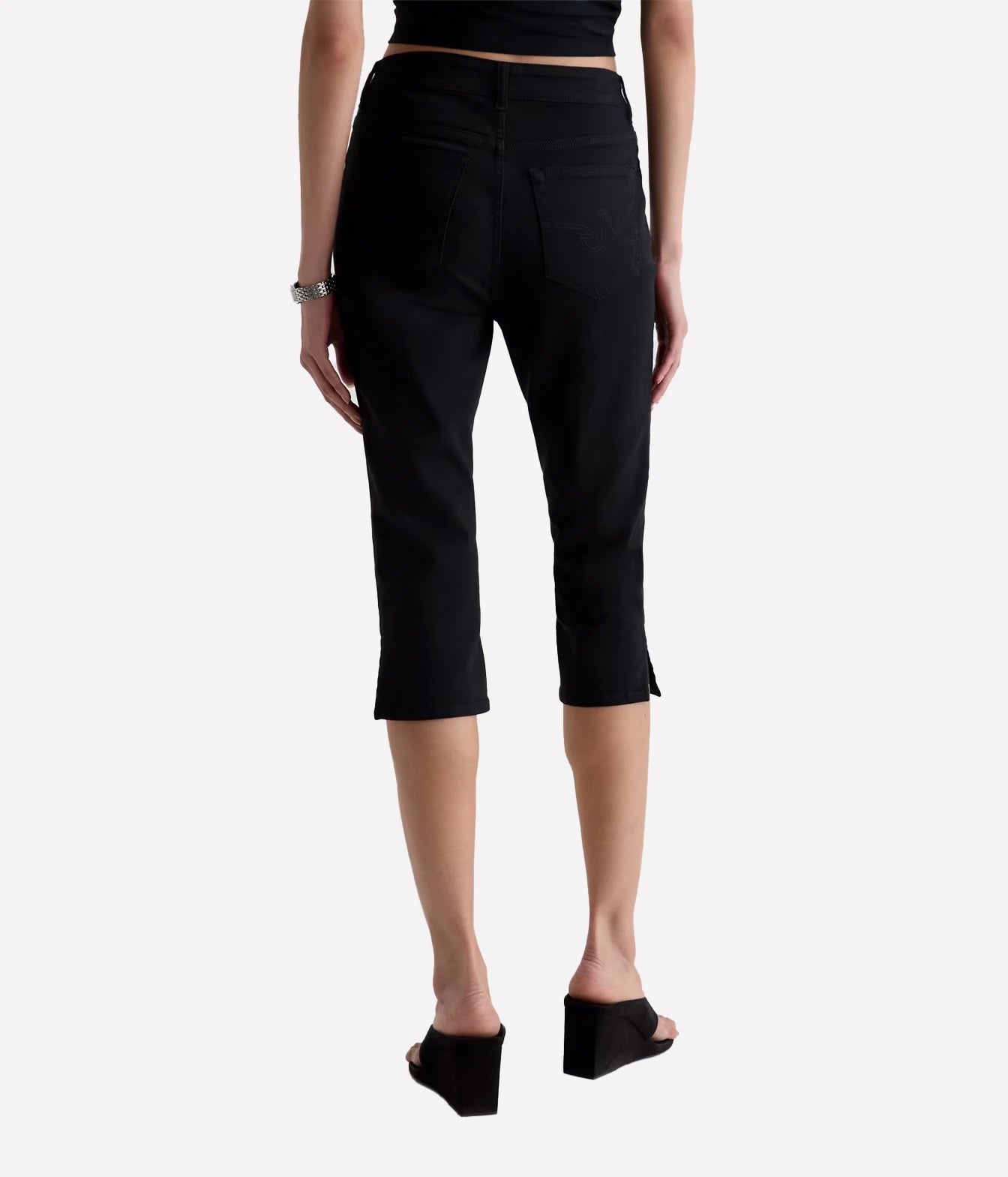 A model shown from the back wearing black cropped capri pants, a black crop top, and black wedge sandals against a light gray studio background.
