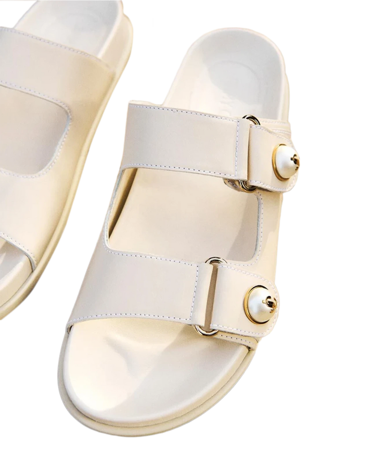 A pair of off-white double-strap slide sandals with gold-tone metal hardware and pearl-like decorative accents on the straps, shown on a clean white background.