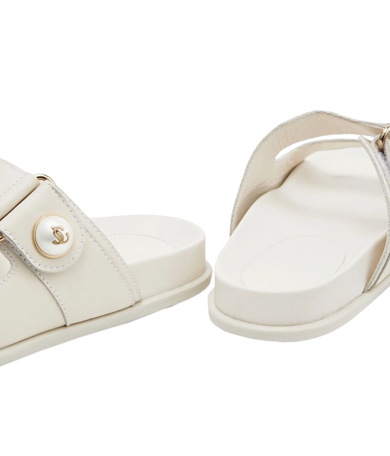 A pair of off-white leather slide sandals with a decorative round button featuring an interlocking CC logo, shown on a clean white background.