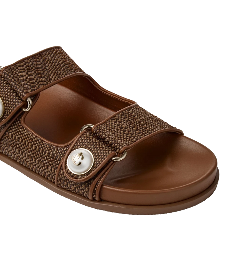 A brown slide sandal with a woven fabric strap and a large silver snap button, shown on a plain white background.