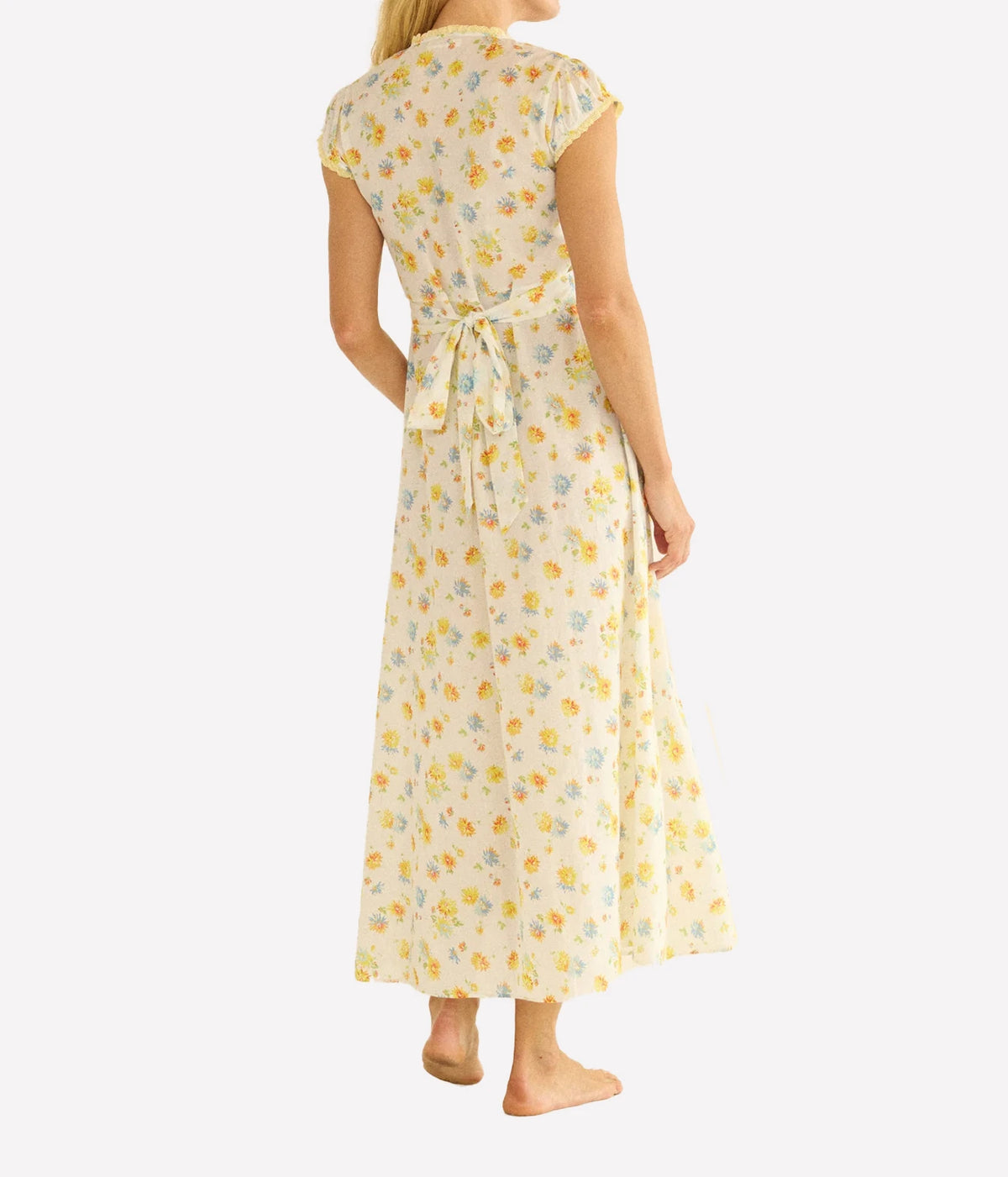 A woman shown from the back wearing a cream-colored midi dress with a yellow and light blue floral print, featuring cap sleeves and a tie waist.