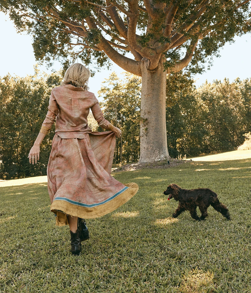 Pierre-Louis Mascia Aloe Silk Skirt in Terracotta Multi, worn on model with the matching Aloe Shirt and black boots, holding out the skirt as a spaniel runs past