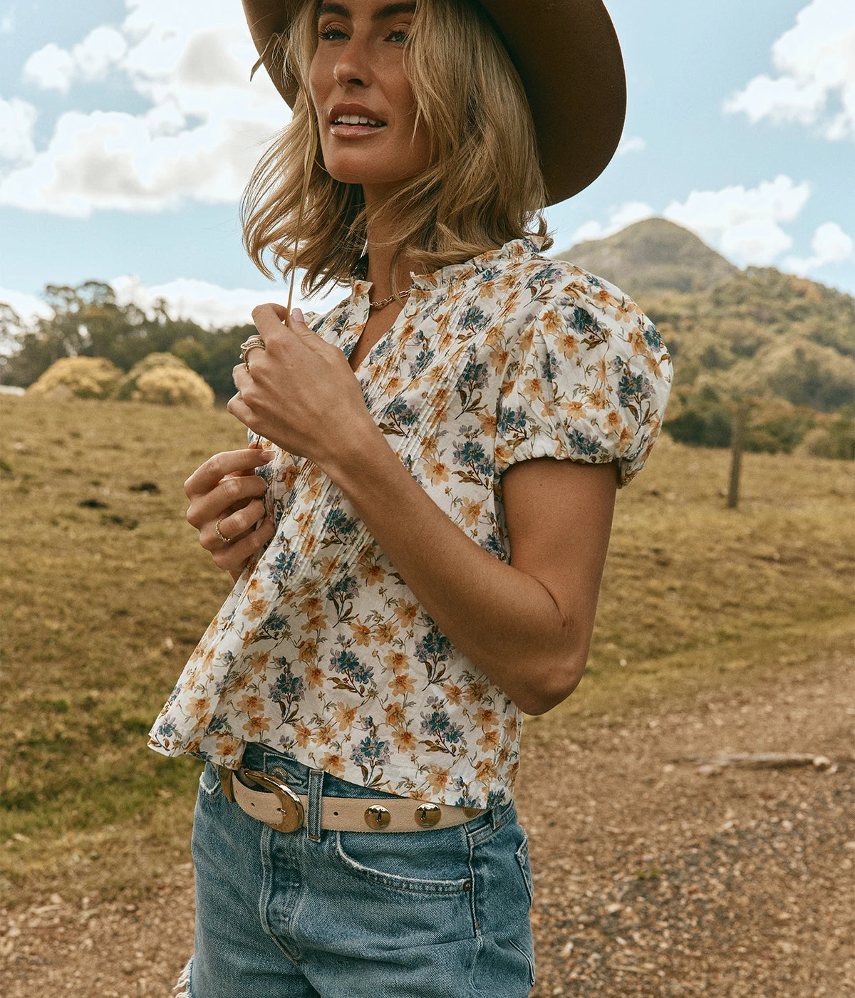 DÔEN Millie Top In Narcissus Bloom, worn on model with denim shorts and a wide-brim felt hat, hand at the neckline