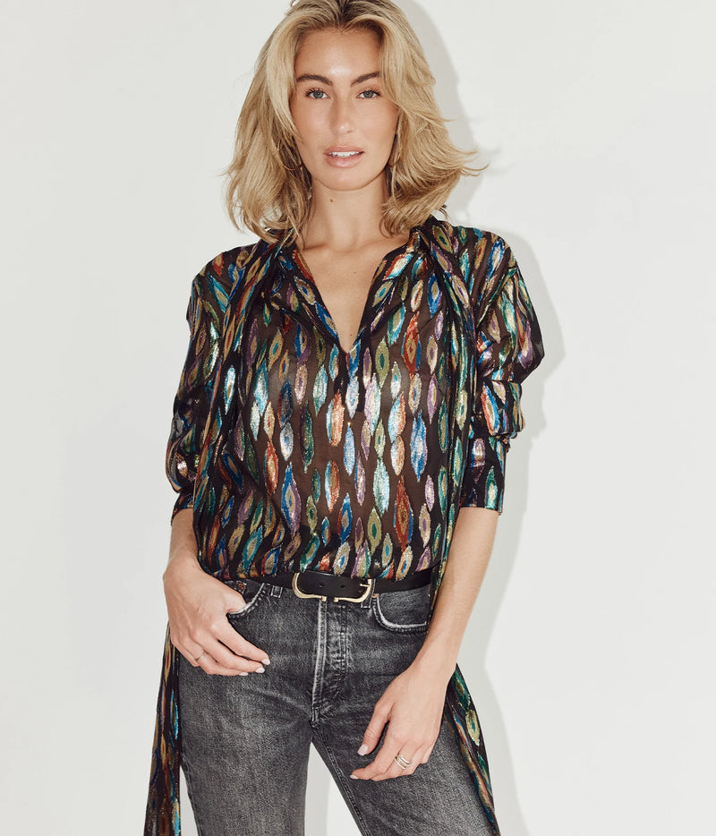 A woman modeling a sheer long-sleeve button-up blouse with a multicolor vertical leaf-like pattern in brown, blue, green, and white over a black base, paired with dark gray jeans and a black belt against a plain white background.