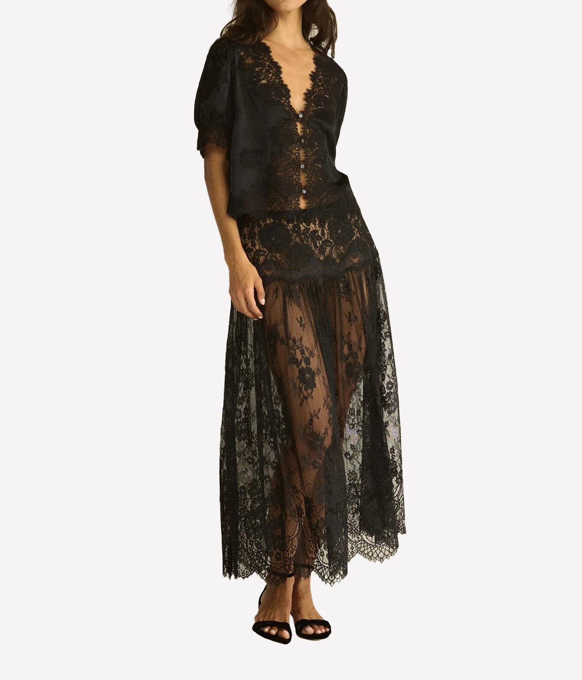 Full-length front view of a model wearing the DÔEN Idella Top In Black buttoned over a sheer black lace maxi skirt with black strappy heels
