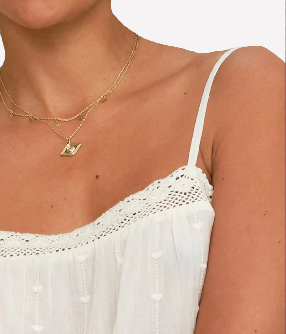 A close-up of a model wearing a white bohemian-style spaghetti strap top. MABE Alli Embroidered Cami In Ecru