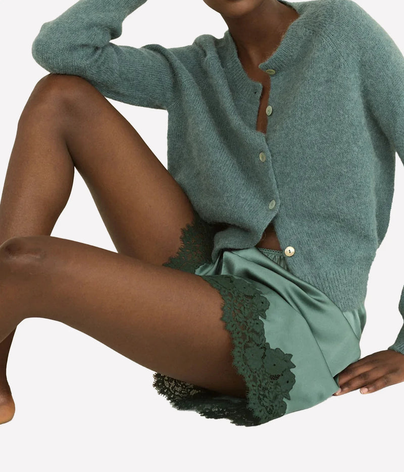 A model wearing a sage green button-up cardigan and DÔEN Irsa Short in Dulac Green with a dark green lace hem.