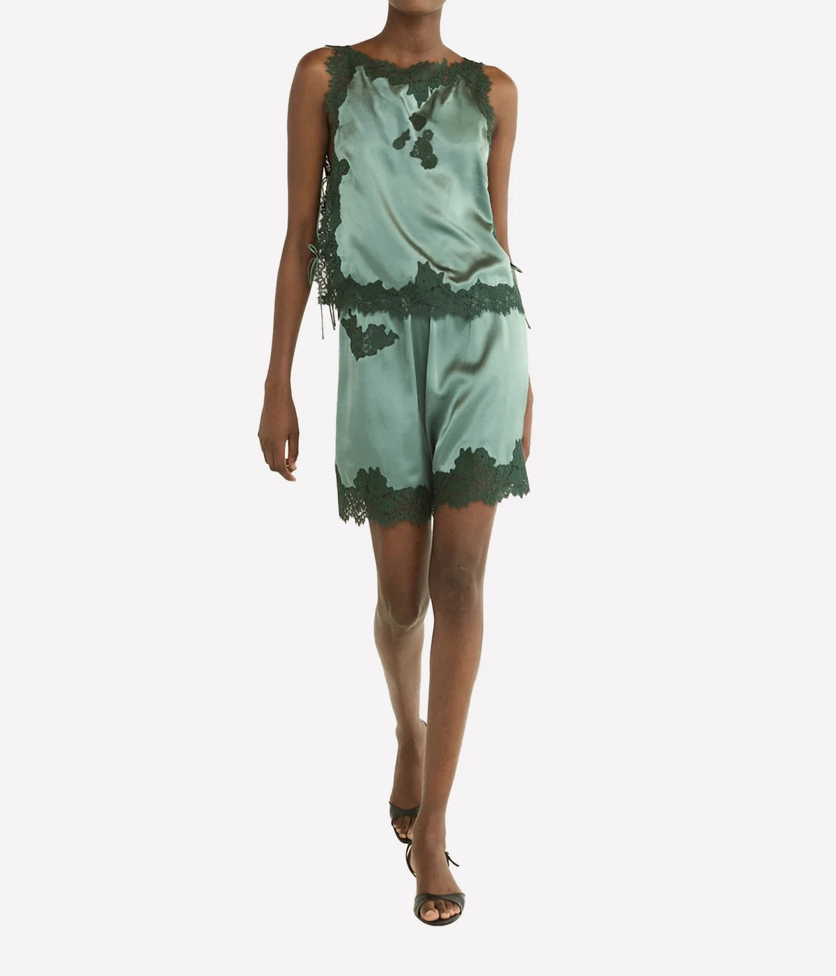 A model wearing a sage green satin romper with dark green lace trim, set against a plain light gray background.