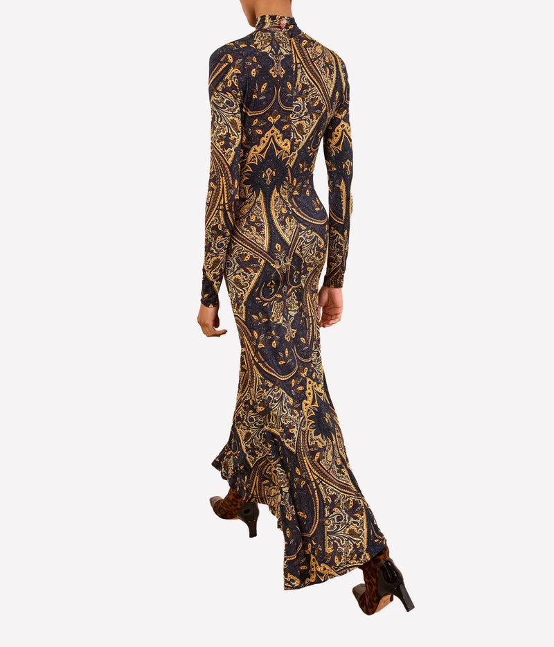 A woman modeling a long-sleeve, high-neck maxi dress with a dark navy and gold baroque pattern, shown from the back against a light gray background.