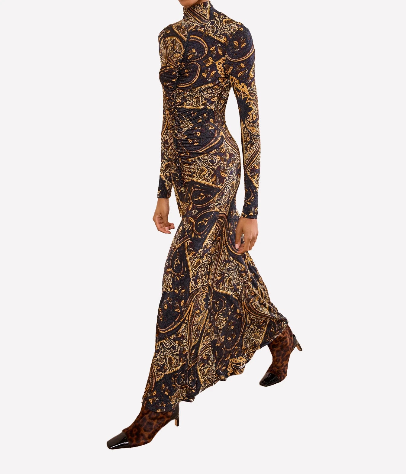 A long-sleeve high-neck maxi dress with an intricate gold and brown baroque-style paisley pattern on a black base, shown on a model against a light gray background.