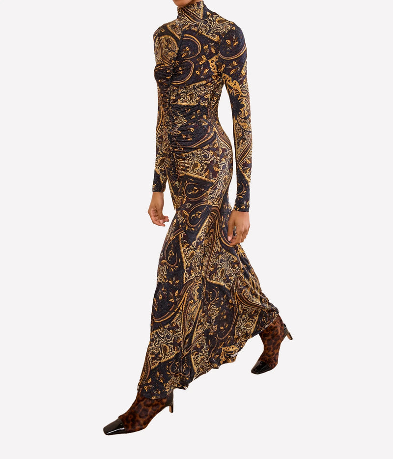 A long-sleeve high-neck maxi dress with an intricate gold and brown baroque-style paisley pattern on a black base, shown on a model against a light gray background.