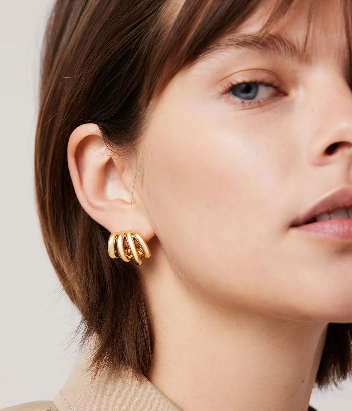 Model with shoulder-length brown hair tucked behind her ear wearing the Jenny Bird Monroe Earrings in Gold, shown from a three-quarter angle