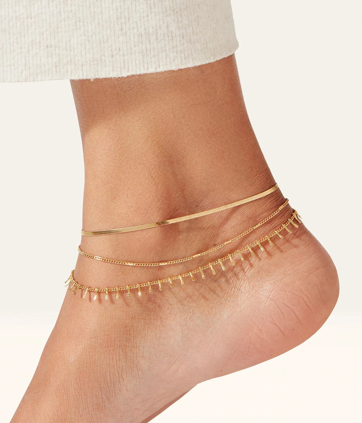 Close-up of the Jenny Bird Surfside Anklet in Gold worn with the heel lifted, showing the strands sitting across the ankle bone