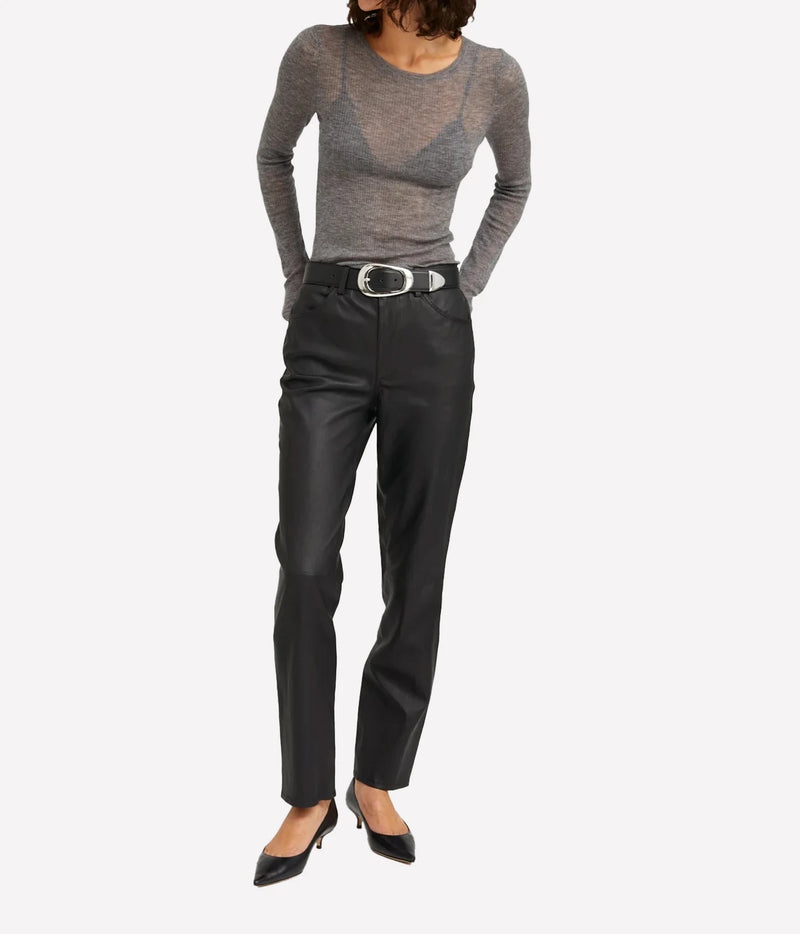 A model wearing a gray long-sleeve knit top, black leather trousers with a silver-belt, and black pointed-toe heels, shown against a plain light gray studio background.