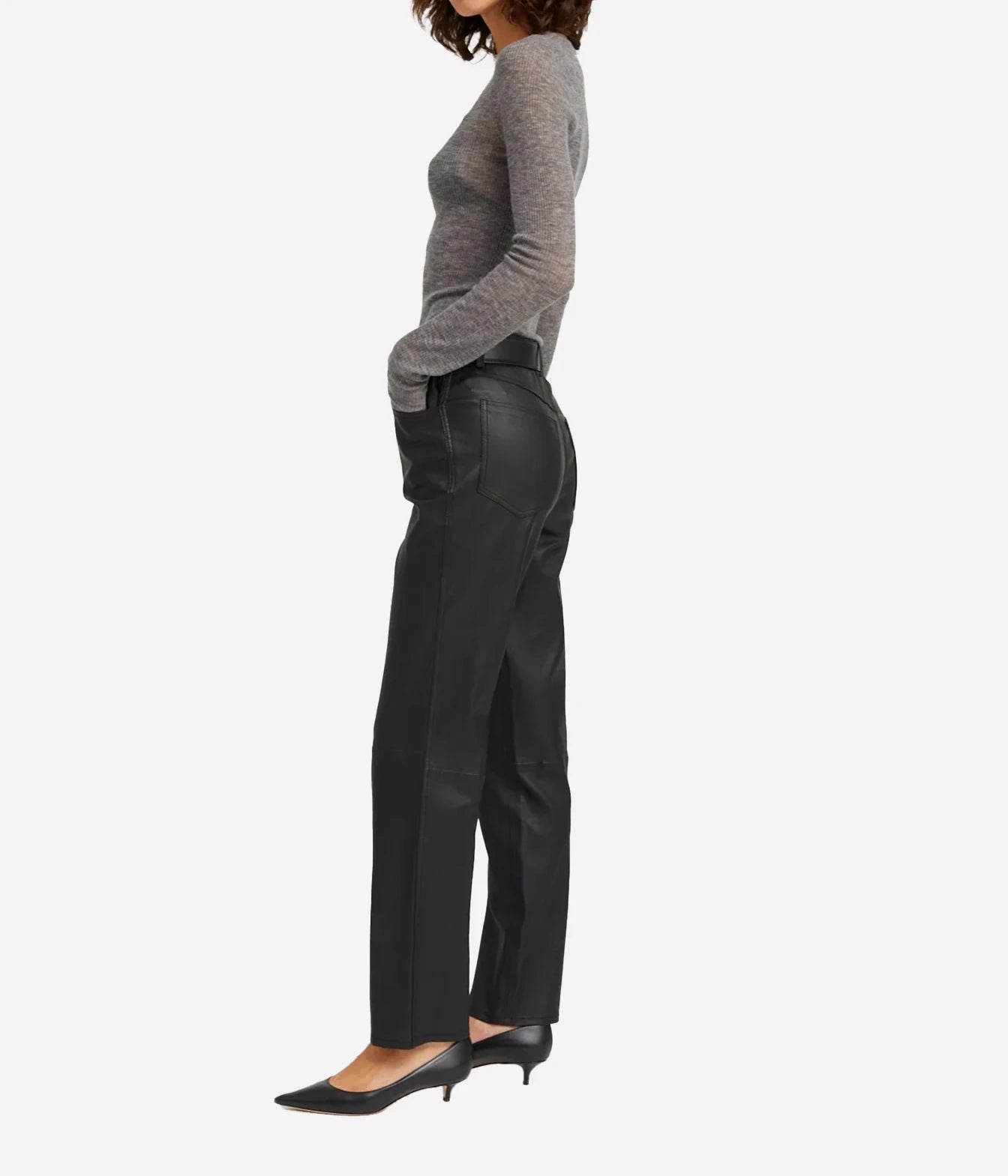 A side-profile view of a model wearing black leather-look straight-leg trousers, a gray knit long-sleeve top, and black pointed-toe heels against a plain light gray background.