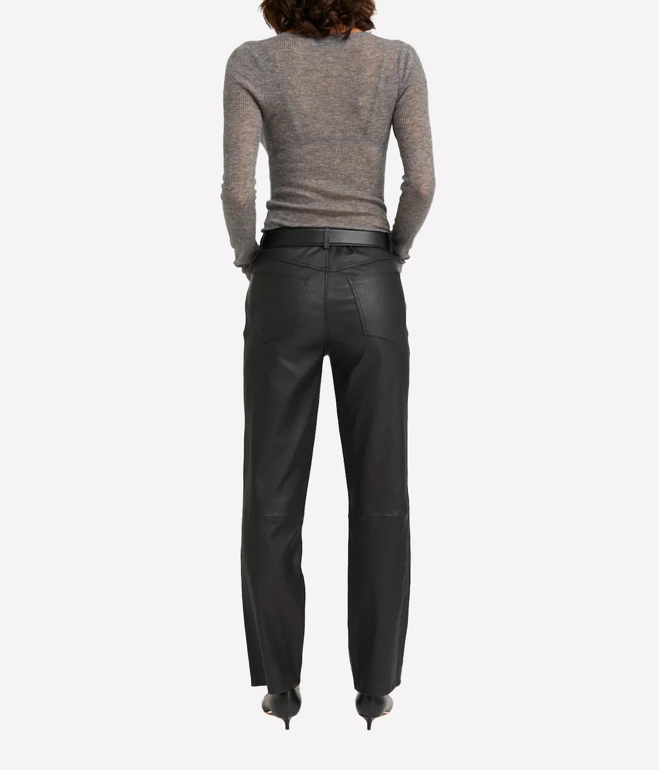Rear view of a model wearing black leather trousers and a gray knit sweater against a light gray background.