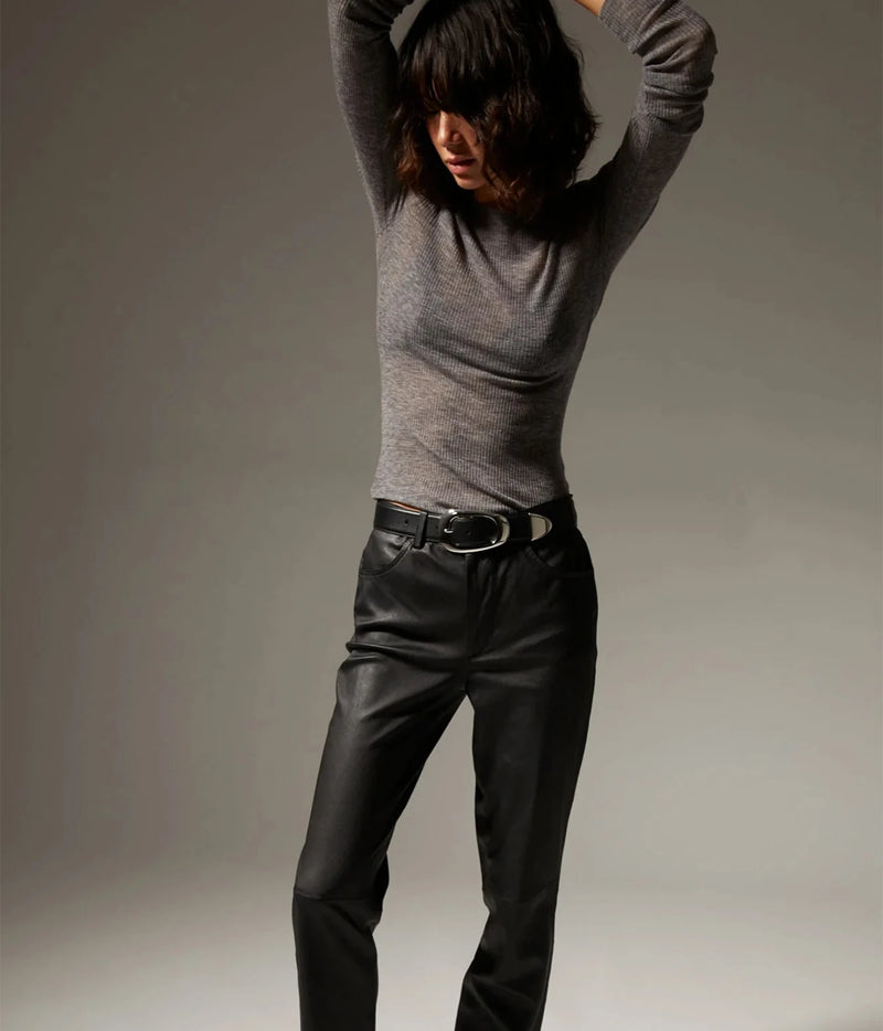 A model wearing a fitted gray long-sleeve knit top and black leather pants with a black belt, posed against a neutral gray studio background.