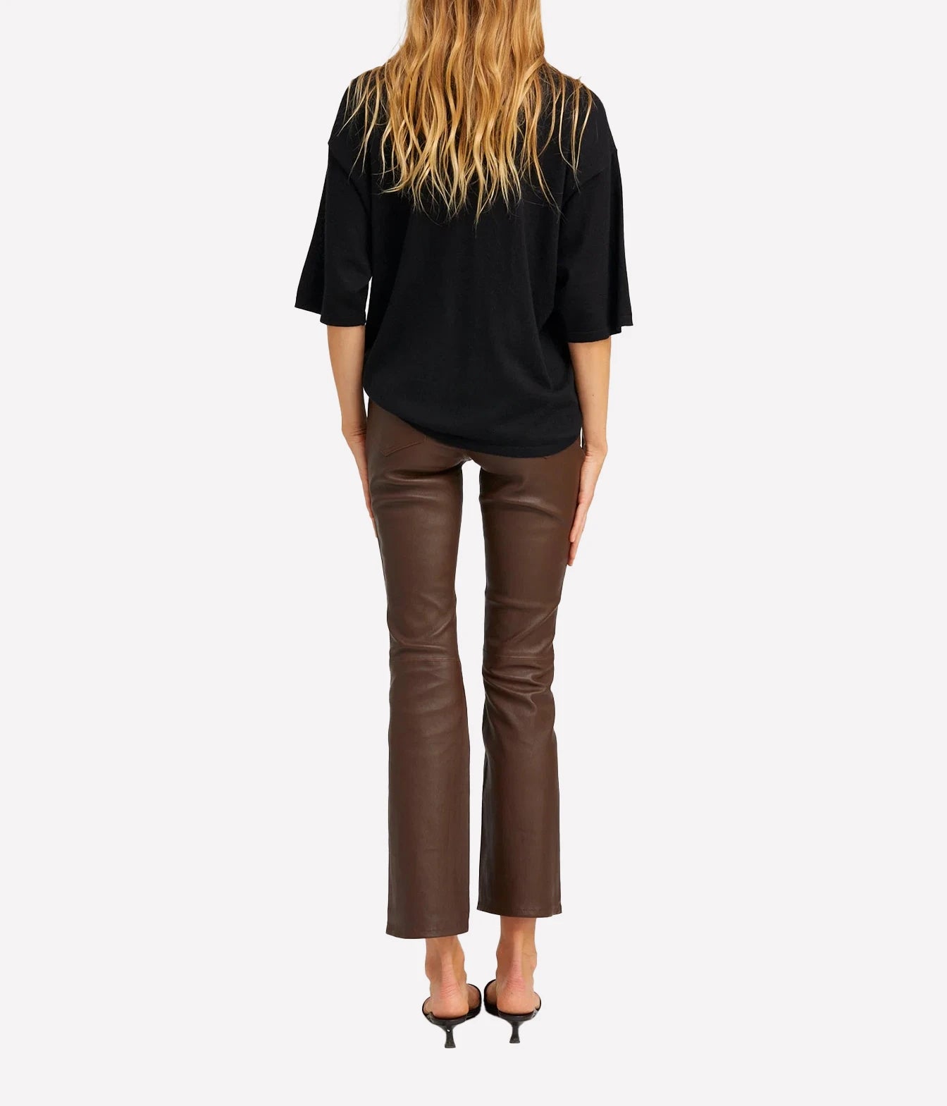 A woman shown from the back wearing a black short-sleeve top, brown cropped flare pants, and black high-heeled sandals against a light gray studio background.