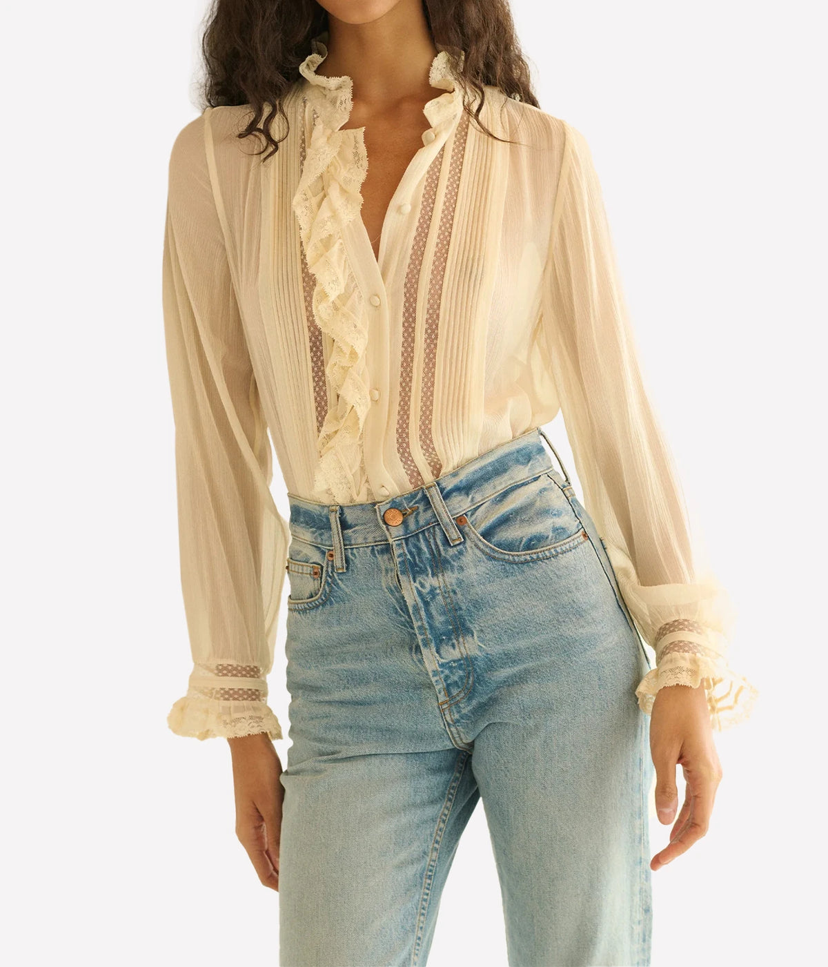 Close front view of a model wearing the DÔEN Magdeleine Top In Candlelight tucked into high-rise light-wash jeans, showing the ruffle front and sheer sleeves