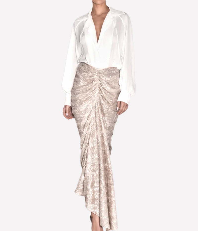 A model wearing a white satin long-sleeve blouse and a shimmering champagne sequined ruched maxi skirt, shown against a plain light gray studio background.