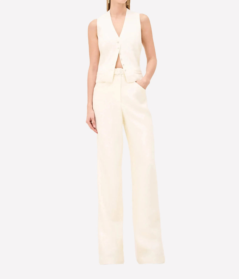 A model wearing a cream-colored sleeveless vest and matching wide-leg trousers, shown against a plain light gray studio background.
