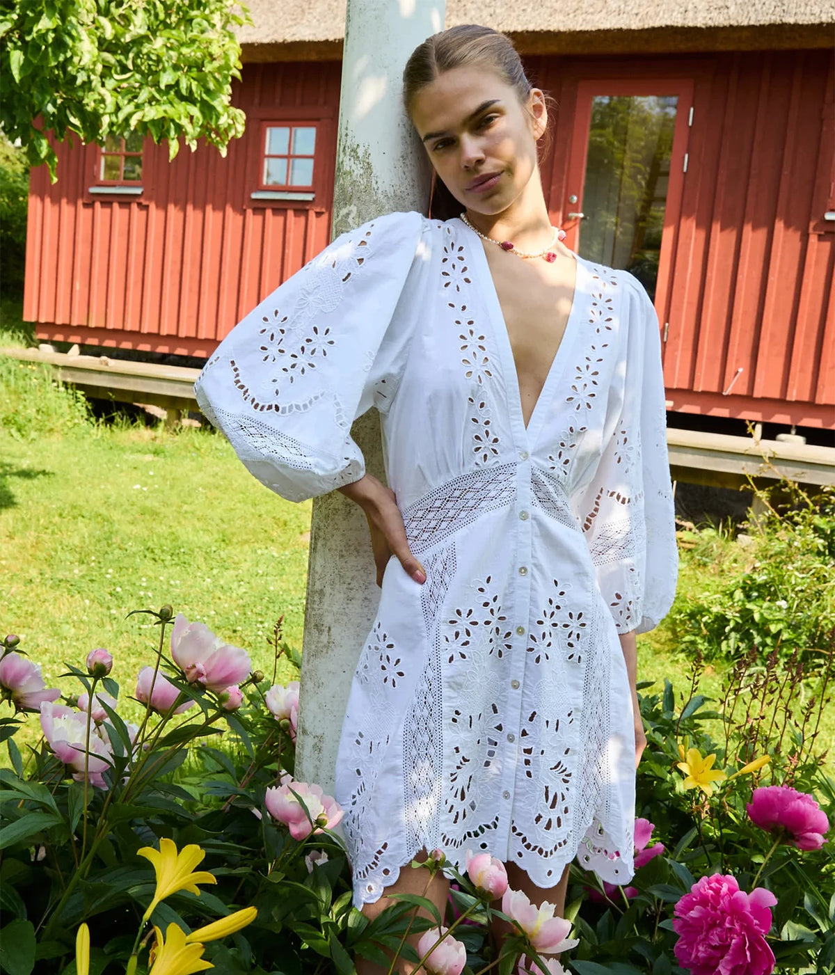 Model wearing the Sissel Edelbo Mila Short Dress in Ecru with one hand at the waist, showing the deep V-neckline, elbow-length balloon sleeves and cutwork embroidery