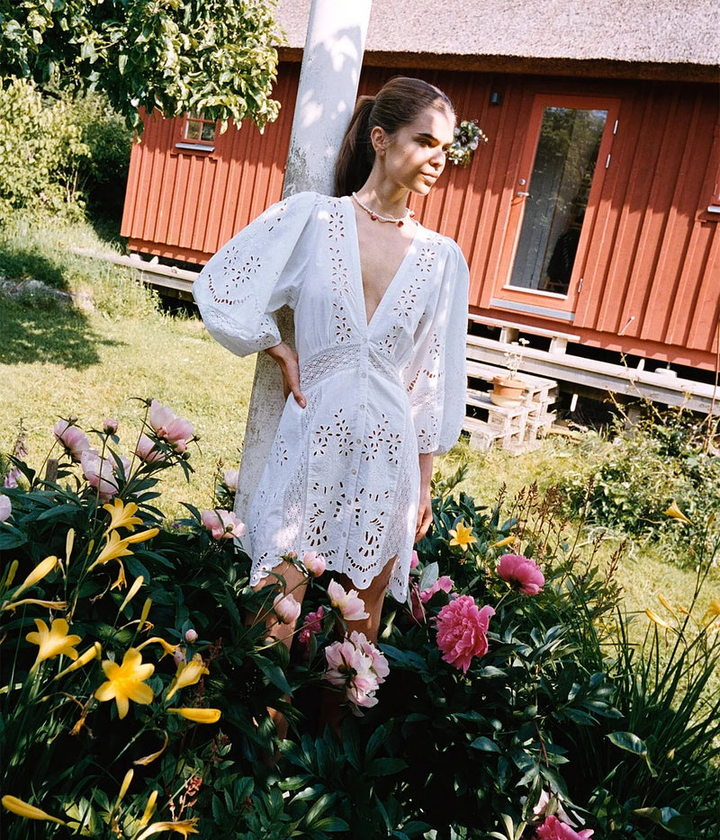 Full-length view of a model wearing the Sissel Edelbo Mila Short Dress in Ecru, showing the short length, gathered waist, balloon sleeves and wavy lace-edged hem