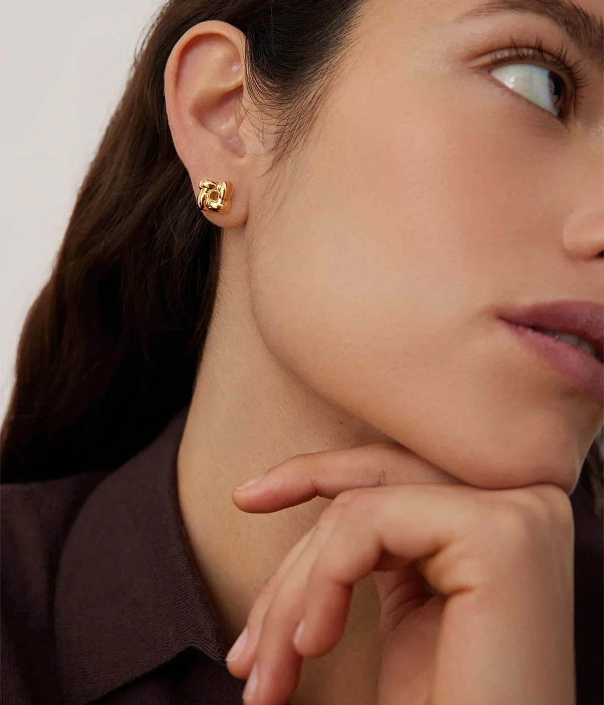 Model resting her chin on her hand wearing the Jenny Bird Mini Woven Square Earrings in Gold with a brown top