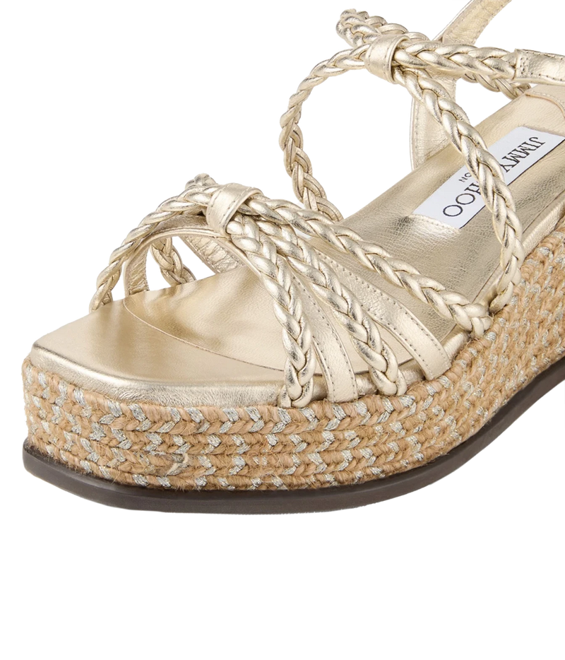 A close-up of a metallic gold platform espadrille sandal with braided straps and a woven jute platform sole, featuring a visible Jimmy Choo insole label.