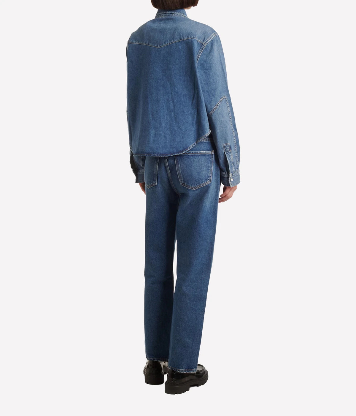 Back view of a model wearing the Citizens Of Humanity Cropped Western Shirt in Chaya with matching mid-wash straight-leg jeans and black loafers, showing the back yoke and cropped hem