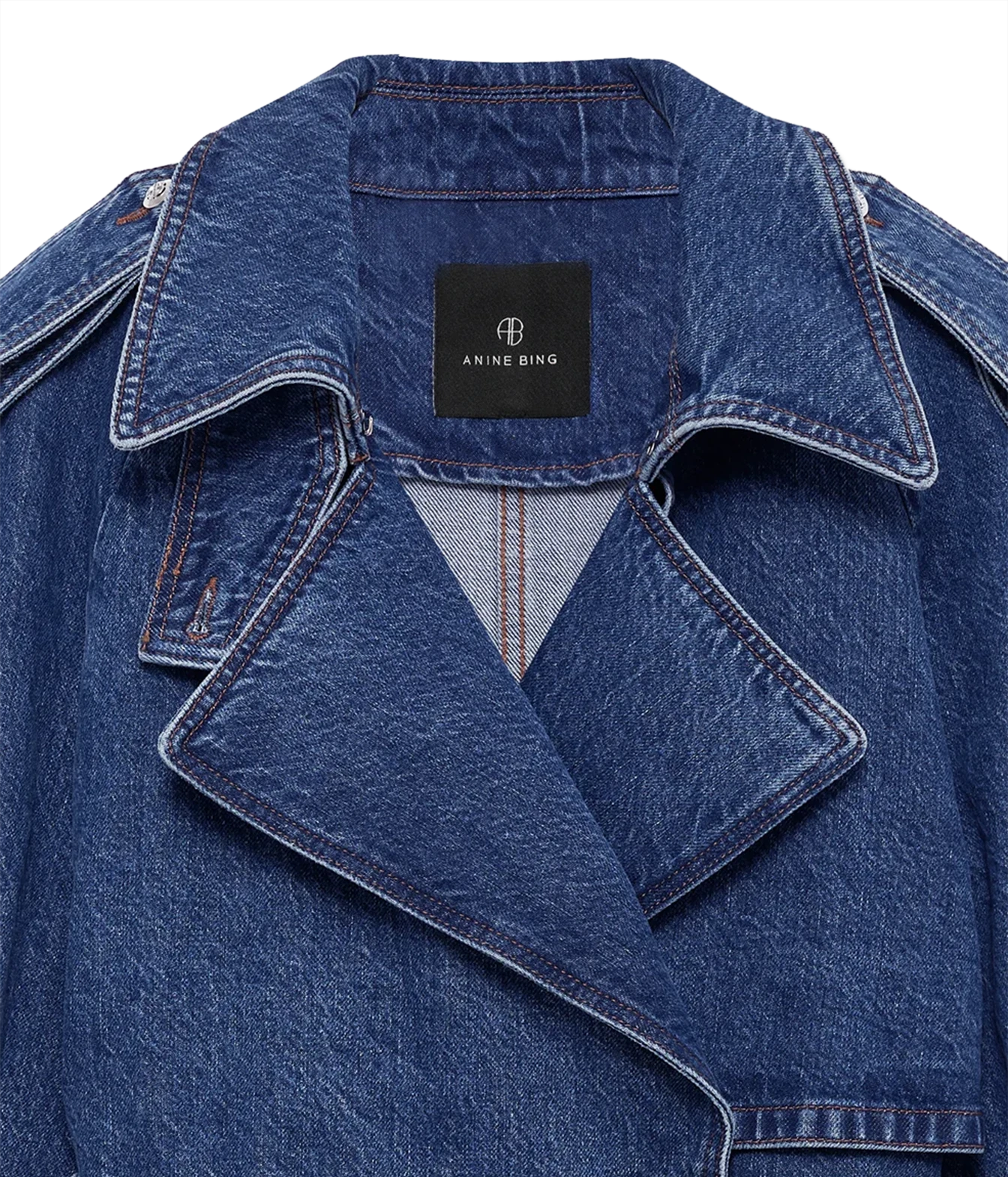 Close-up of a blue denim jacket with a black Anine Bing brand label on the collar, showing the textured denim fabric and contrast stitching.
