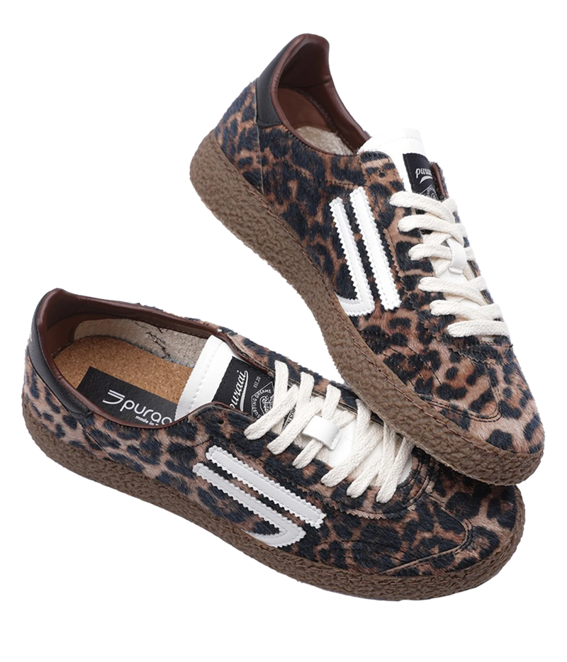 A pair of Puraai low-top sneakers featuring a brown and black leopard print canvas upper, white laces, and white side stripes, set against a plain white background.