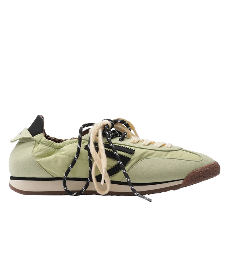 A light green low-top sneaker with black and white patterned laces, beige laces, a cream midsole, and a brown gum outsole, shown from a side profile on a white background.