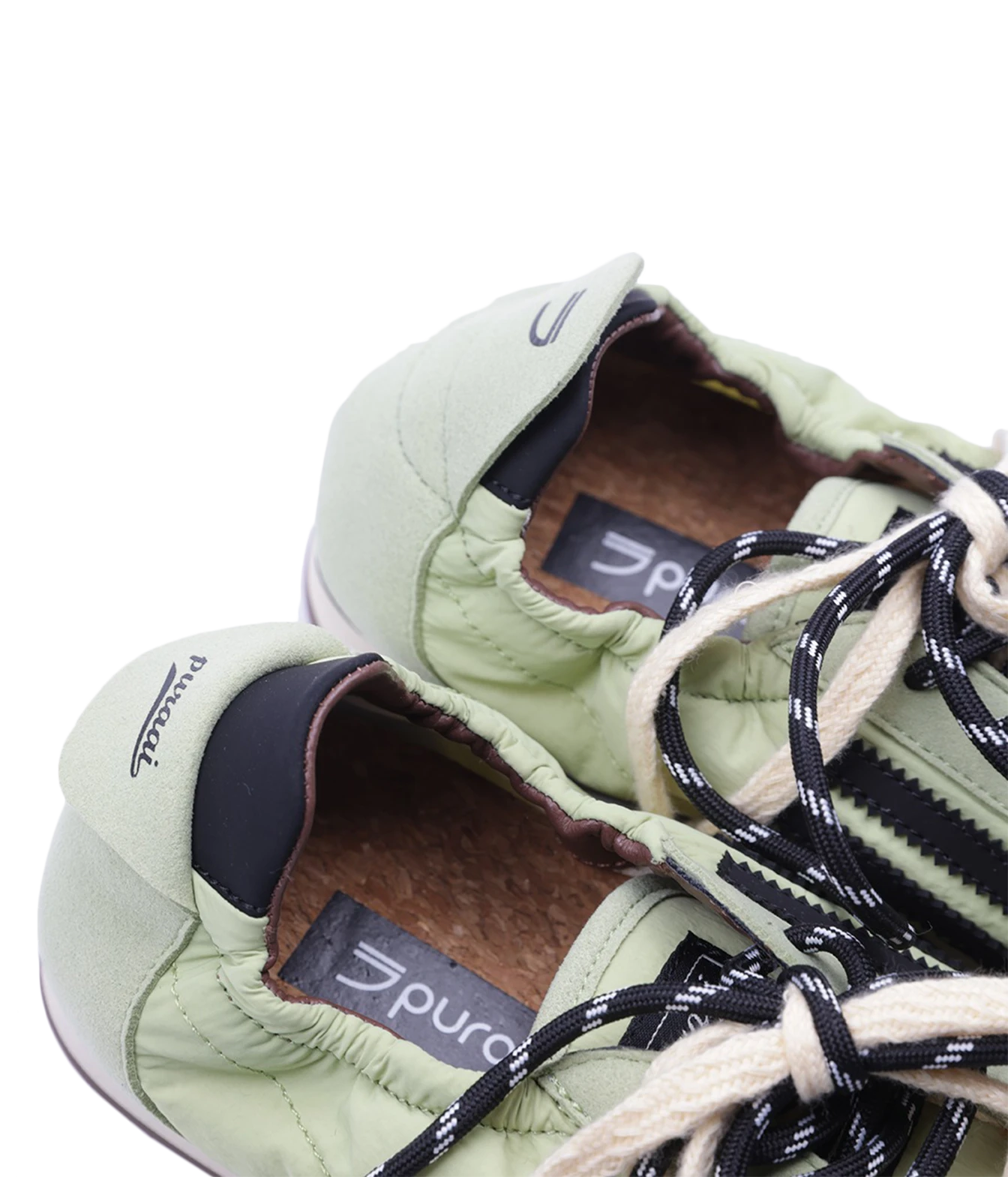 Close-up of a pair of light sage green puffer sneakers with black and white laces, showing the interior lining and branding.