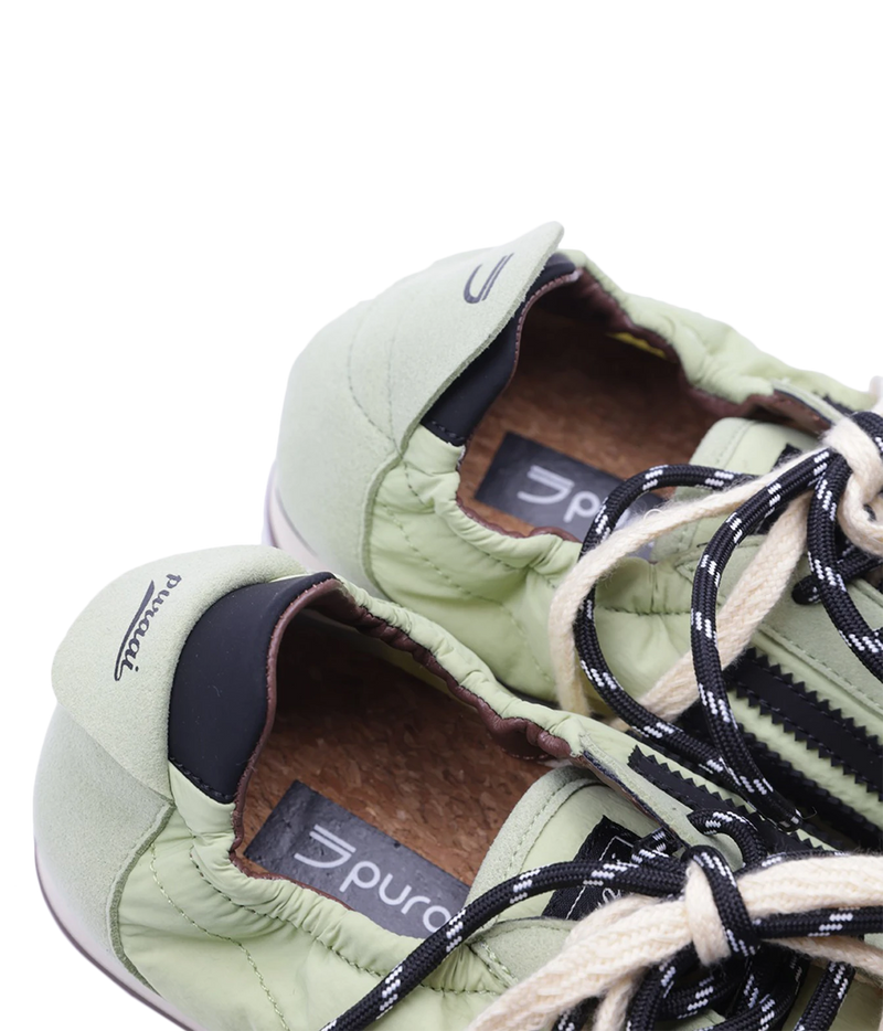 Close-up of a pair of light sage green puffer sneakers with black and white laces, showing the interior lining and branding.