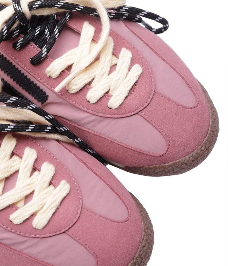 Close-up of a dusty pink sneaker with cream-colored laces and black-and-white patterned shoelaces, set against a plain white background.