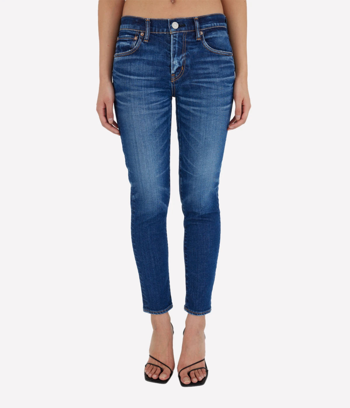 Dark blue skinny jeans with a low-rise waist and ankle-length fit, styled with a white blouse and heels for a chic, sophisticated look.
