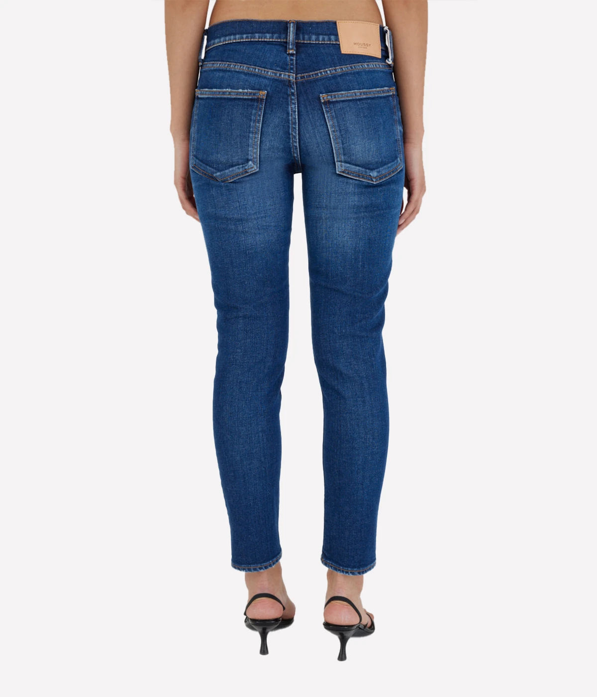Dark blue skinny jeans with a low-rise waist and ankle-length fit, styled with a white blouse and heels for a chic, sophisticated look.